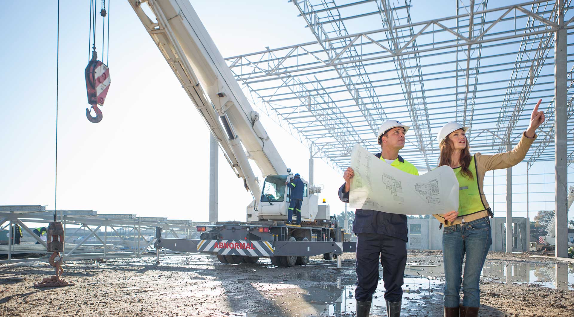 two people looking at Construction blueprints on a job site with a crane in the background